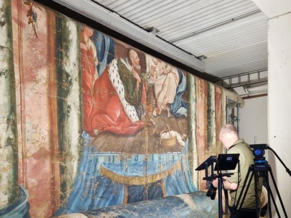 Ett stativ med kamera står framför en stor altartavla som håller på att nedmonteras.