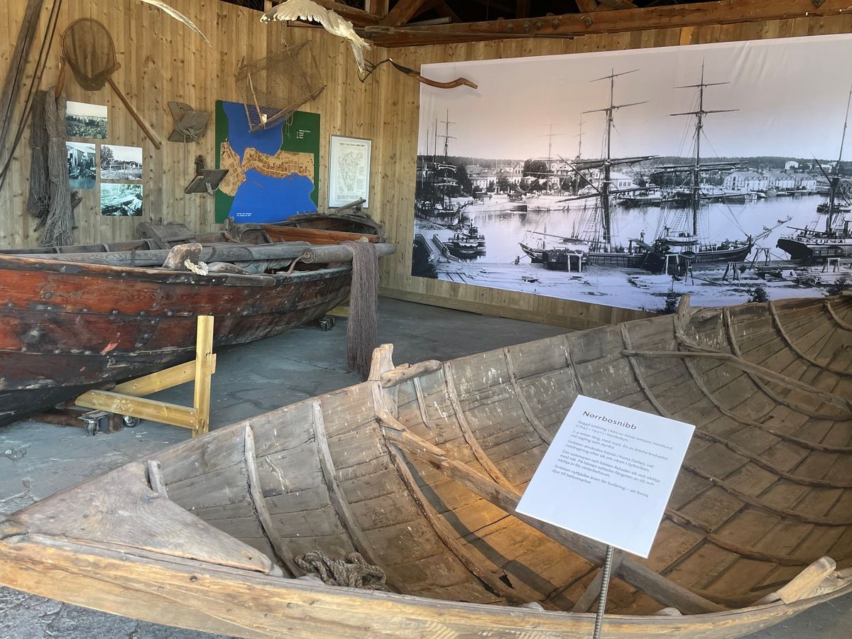 Interiör från en utställning med äldre träbåtar och ett stort fotografi över Hudiksvalls hamn
