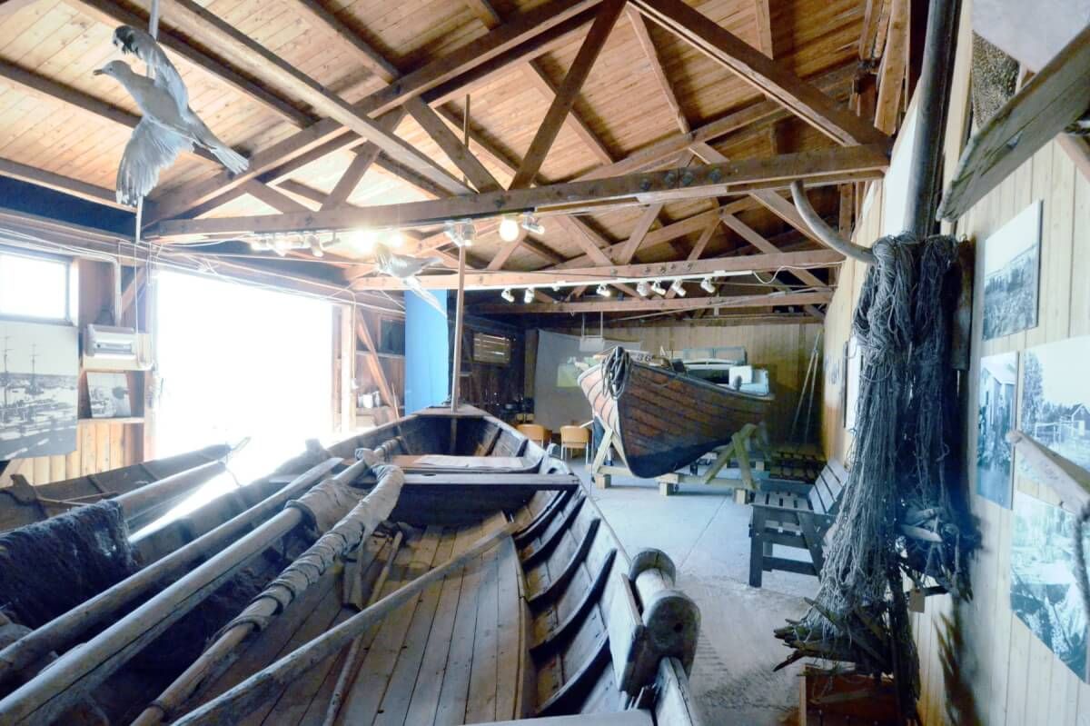 Insidan av Hälsinglands museums båtmagasin med båtar, tampar, fiskenät och bilder av fiskeläger.