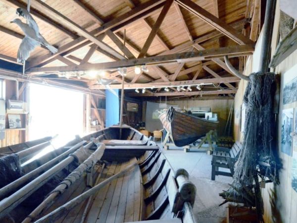 Insidan av Hälsinglands museums båtmagasin med båtar, tampar, fiskenät och bilder av fiskeläger.