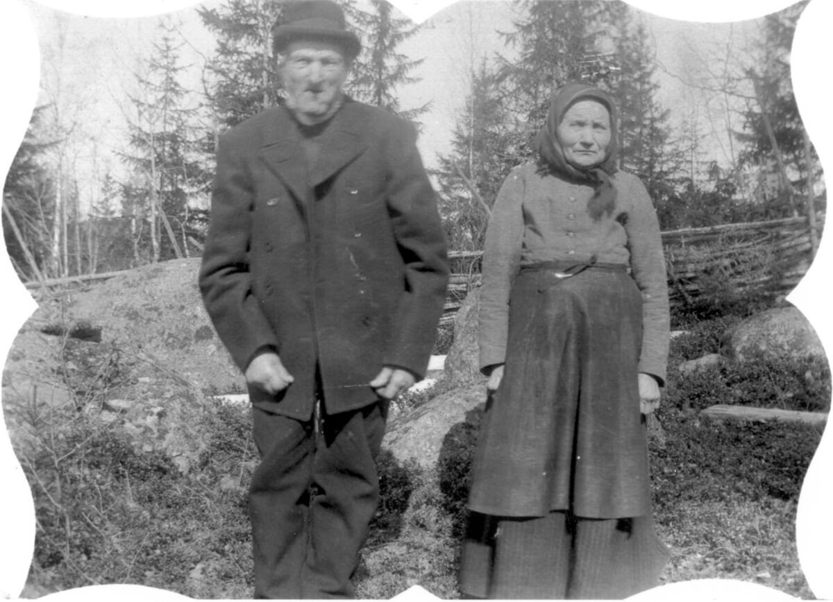 Man och hustru poserar utomhus framför en gärdesgård.