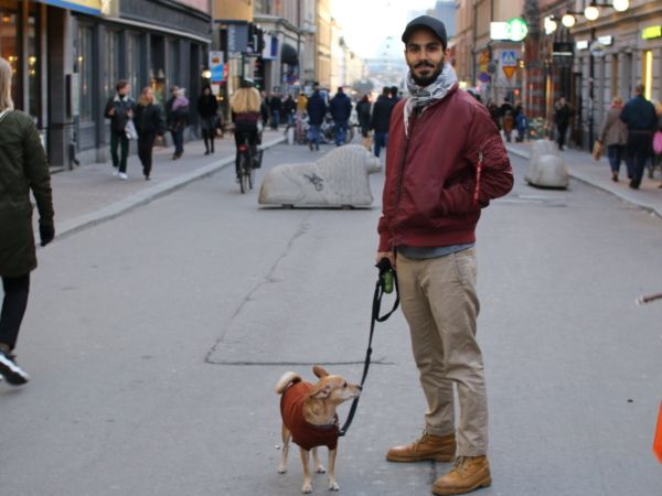 En man med hund står på gågata.