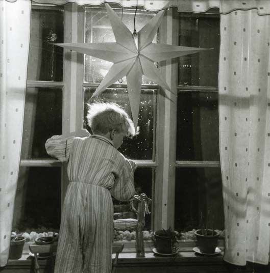 Undrar just vart tomten tog vägen? En liten pojke i randig pyjamas står på en stol och tittar ut genom ett fönster där det hänger en julstjärna av papper, julen 1949. På fönsterbrädan står en halmbock och mellan fönsterrutorna ligger vitlav.
