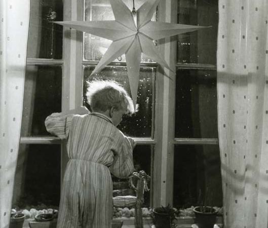 Undrar just vart tomten tog vägen? En liten pojke i randig pyjamas står på en stol och tittar ut genom ett fönster där det hänger en julstjärna av papper, julen 1949. På fönsterbrädan står en halmbock och mellan fönsterrutorna ligger vitlav.