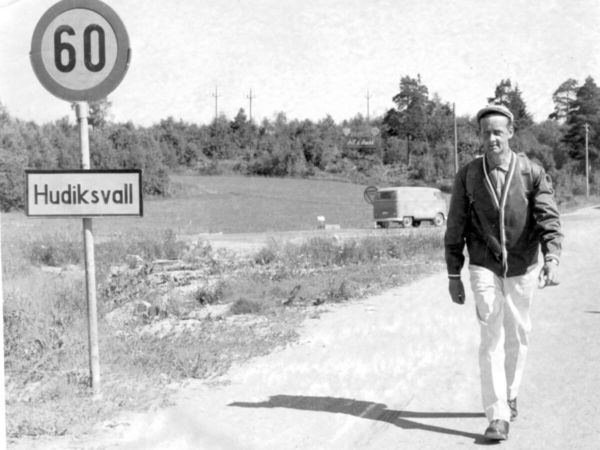 En man går längs en väg och till vänster om honom står "Hudiksvall" på en skylt.