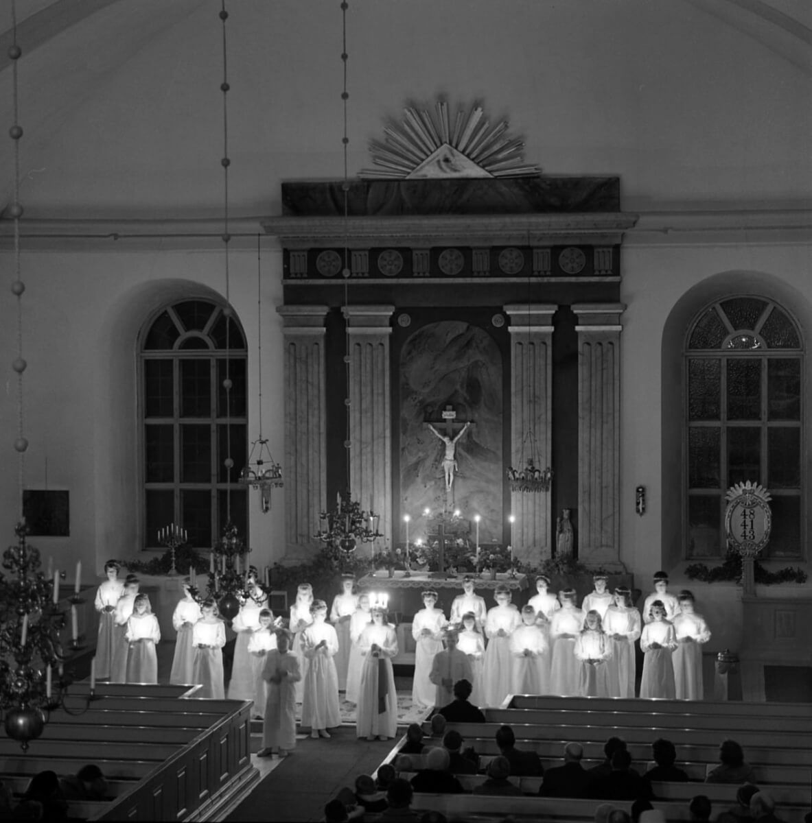 Ett luciatåg med tända ljus står uppställda längst fram i en kyrka.