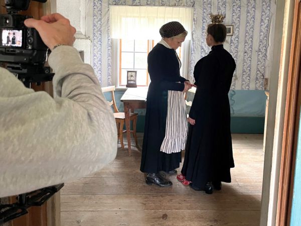 Två personer i 1800-talskläder filmas i en hälsingegård