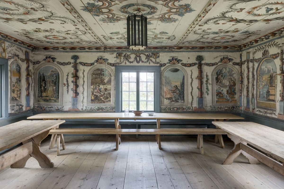 Festsal, s.k. herrstuga med målningar på väggarna möblerat med långbord och bänkar.