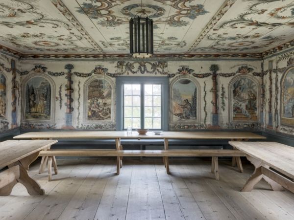 Festsal, s.k. herrstuga med målningar på väggarna möblerat med långbord och bänkar.