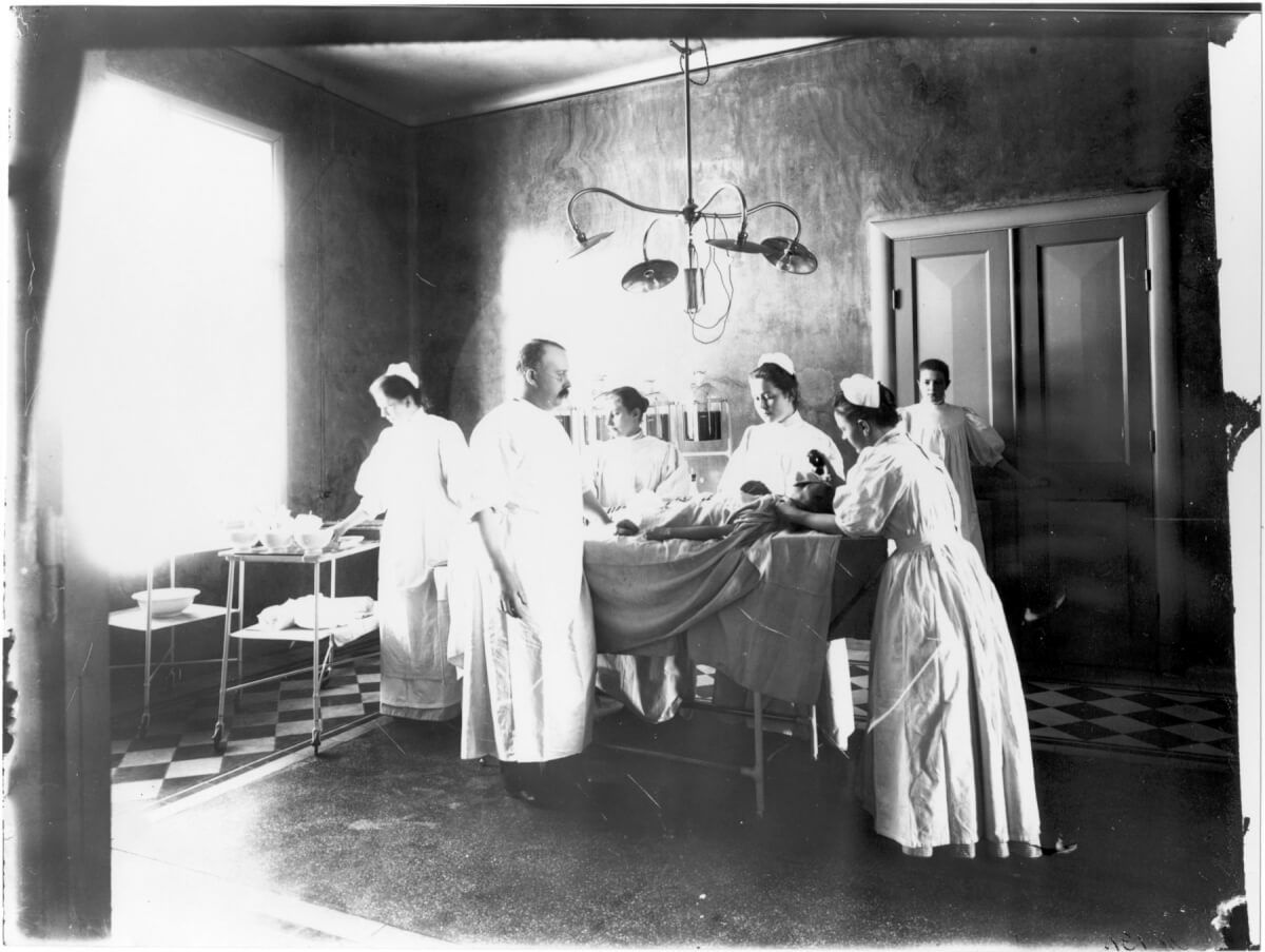 En läkare och fem sjuksköterskor i en operationssal. En patient ligger på operationsbordet.