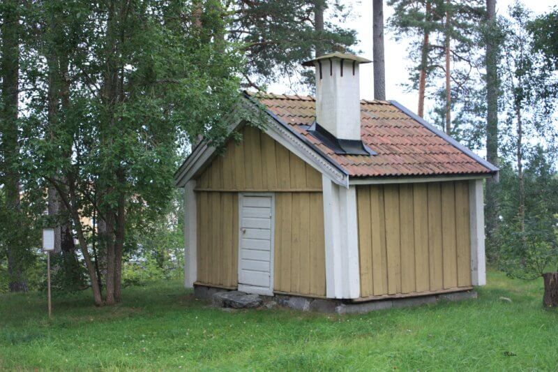 Stuga med skorsten en grönskande sommardag.