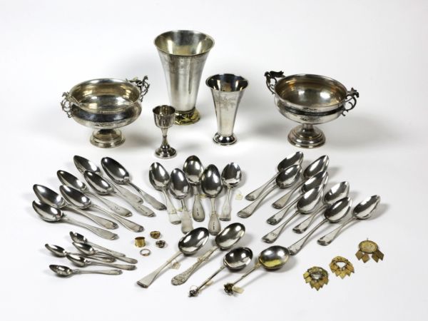 En samling silverföremål. Längst bak bägare, skålar, m.m. I nederkant silverskedar och smycken.