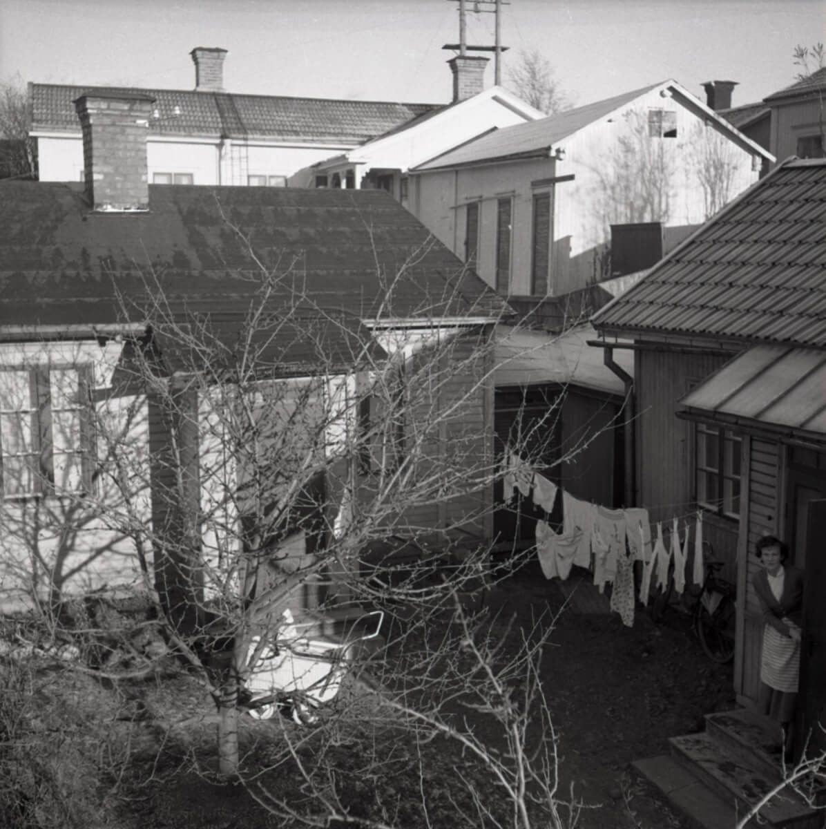 En stadsinnergård med upphängd tvätt på en tvättlina samt en kvinna som tittar ut genom en dörröppning.